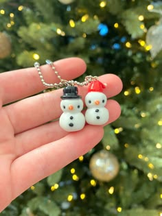 two snowmen wearing hats and scarfs are shown on a small keychain in front of a christmas tree