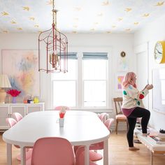 a woman standing in the middle of a room with pink chairs and a white table