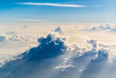 the view from an airplane looking down at clouds and sun beams in the sky above