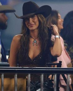 a woman wearing a cowboy hat and black dress sitting next to a man in a crowd