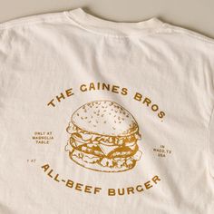 Show off your support for one of the best burgers in town with this classic ivory tee! Inspired by the fan-favorite Gaines Brothers Burger at Magnolia Table, this white tee features a playful, contrasting burger graphic that reads THE GAINES BROS ALL-BEEF BURGER. Restaurant Tshirt Designs, Graphic Tee Inspo Design, Coffee Shop Tshirt, Burger Graphic, The Best Burgers, Best Burgers, Magnolia Table, Beef Burger, Aime Leon Dore