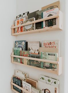 three wooden shelves holding books and magazines on the wall in a room with white walls