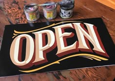 an open sign is sitting on a table with four cans of beer in front of it