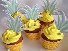 pineapple cupcakes with yellow frosting and green leaves on top are arranged in cones