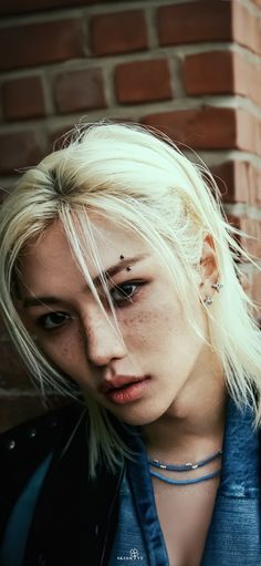 a woman with white hair and piercings standing in front of a brick wall looking at the camera