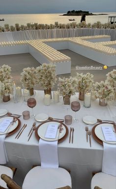 the table is set with white flowers and place settings