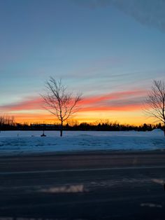 the sun is setting behind some trees in the snow