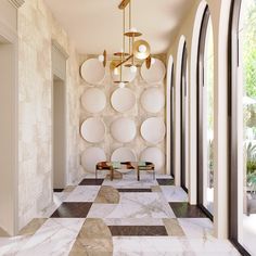 the hallway is decorated in white marble and features circular mirrors on the wall, two tables with stools, and round glass windows