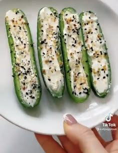 someone holding a white plate with four green peppers on it, topped with cheese and seasoning