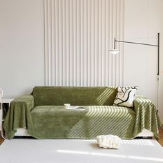 a green couch covered in a blanket next to a white table with two black and white pillows