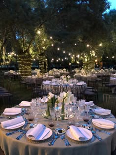 a table set up for an event with white flowers and silverware on it, surrounded by string lights