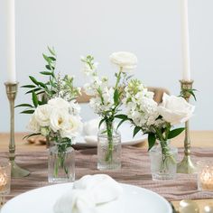 white flowers in glass vases on a table with candles and napkins around it