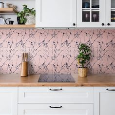 a kitchen with white cabinets and pink wall paper on the back splashing from the backsplash