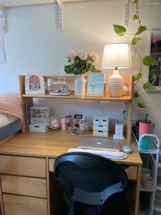 a wooden desk topped with a laptop computer next to a lamp and potted plant