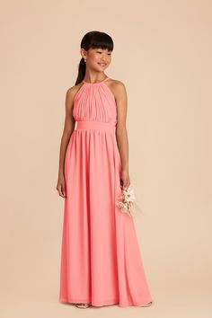 a woman in a long pink bridesmaid dress holding a flower bouquet and smiling at the camera