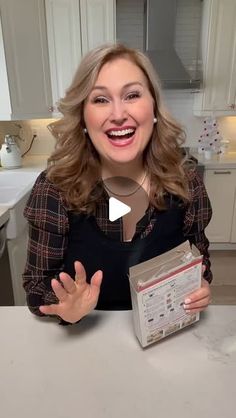 a woman sitting at a kitchen table with an open box in front of her smiling