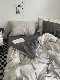 an unmade bed with white sheets and black and white checkerboard flooring