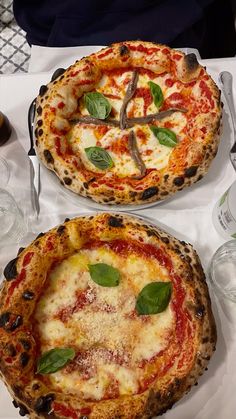 two pizzas sitting on top of a table covered in cheese and basil toppings