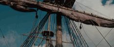 the mast of a tall ship against a blue sky with clouds in the back ground