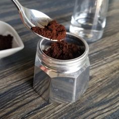 a spoon full of dirt sitting on top of a wooden table next to two cups