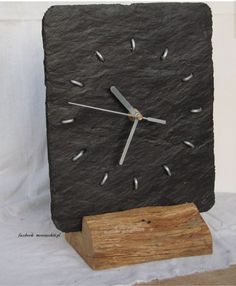 a clock made out of slate sitting on top of a piece of wood next to a wooden block