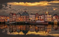 the city is lit up at night with clouds in the sky and reflecting on the water