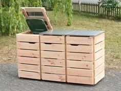 a large wooden box sitting on top of a brick sidewalk next to a tree and grass