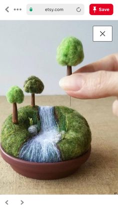 someone is holding their finger over a miniature waterfall in the middle of a small forest