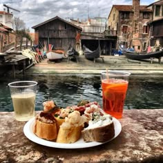 there is a plate with food and drinks on the table next to water in front of some buildings