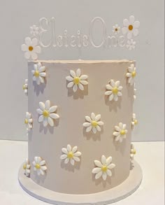 a white cake decorated with daisies and the word elsie's one on top