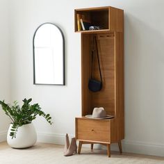 a wooden cabinet sitting next to a white vase with a plant in it and a mirror on the wall