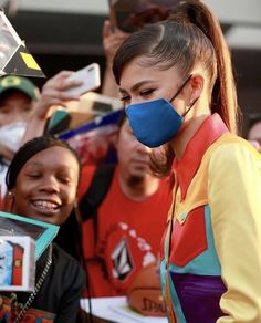 a woman wearing a face mask while standing next to a group of people with cell phones