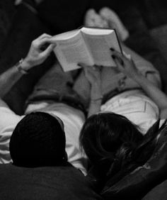 a man and woman laying on a couch reading books