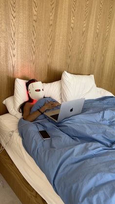 a person laying in bed with a laptop computer on their lap and headphones to their ears