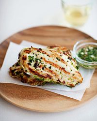 grilled chicken on a wooden plate next to a small bowl of green dipping sauce