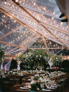 the inside of a tent with tables and chairs set up for a wedding reception under string lights