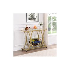 a gold metal and glass bar cart with bottles on it's wheels, in front of a window