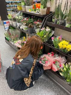 a woman kneeling down to pick up flowers in a flower shop with lots of potted plants