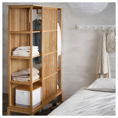 an open bamboo shelf next to a bed with white sheets and blankets on top of it