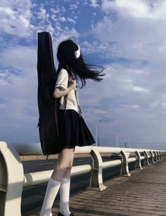 a woman with long black hair and white socks is standing on a bridge looking at her cell phone