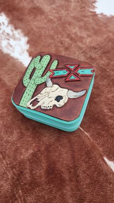 a wallet with a skull and cactus on the front is laying on a cow skin surface