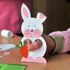 a child holding up a paper bunny with a carrot in it's hand on a table