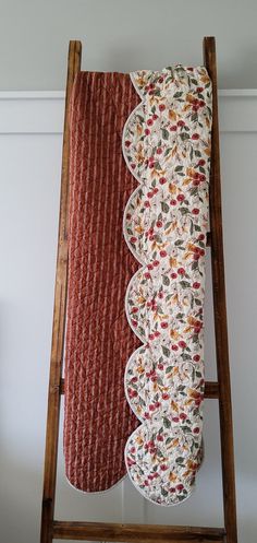 an old wooden ladder with a quilted pillow on it's side and another piece of fabric hanging from the back