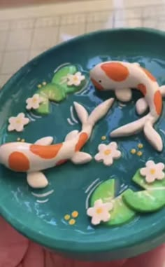 a hand holding a blue bowl with two koi fish in it's center