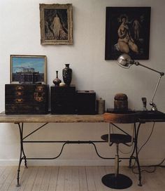 an old desk with antique items on it in front of two paintings and a lamp