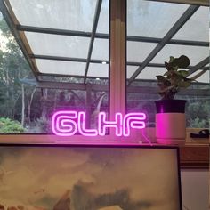 a pink neon sign that reads glff above a painting and potted plant