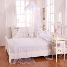 a white bed in a room with wooden floors and windows on both sides is covered by a mosquito net