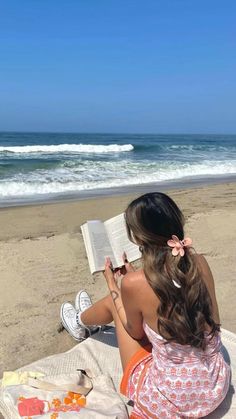 a woman sitting on the beach reading a book