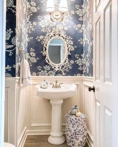 a white sink sitting under a bathroom mirror next to a blue and white wallpaper