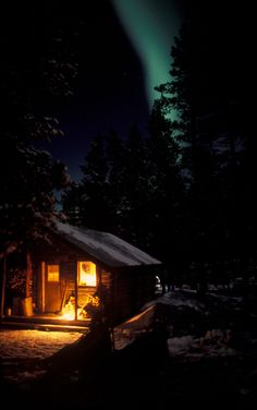 the cabin is lit up at night with an aurora bore in the sky behind it